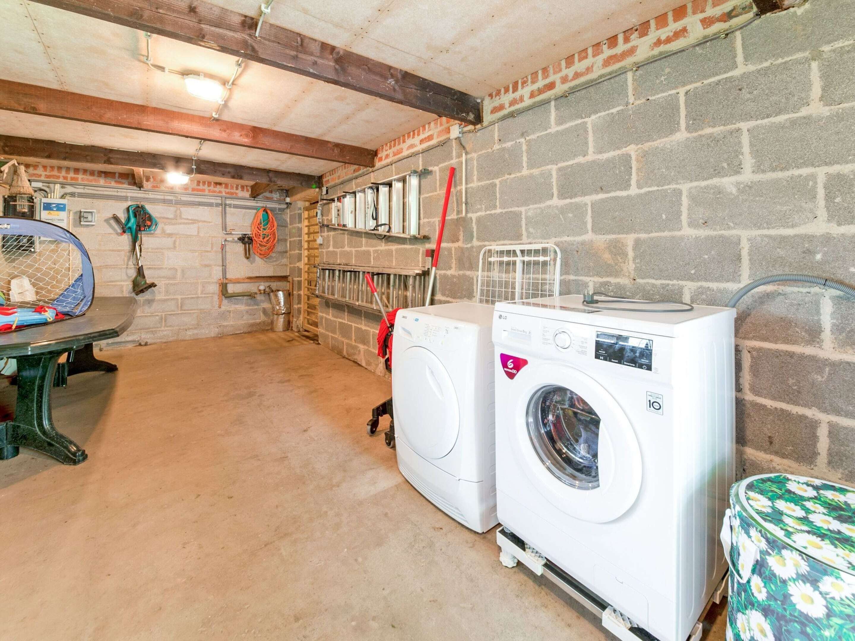 A laundry room with two washing machines, a drying rack, and a table with a basket.