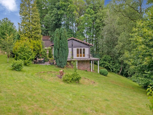 Uma casa com alicerce de pedra, varanda e um jardim com diversas plantas e gramado.