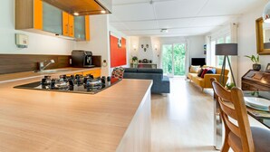 A modern kitchen with a central island, a dining area with a wooden table, and a living room with a sofa and a coffee table. - Cozy Hideaway in Ferrieres (Ferrieres)