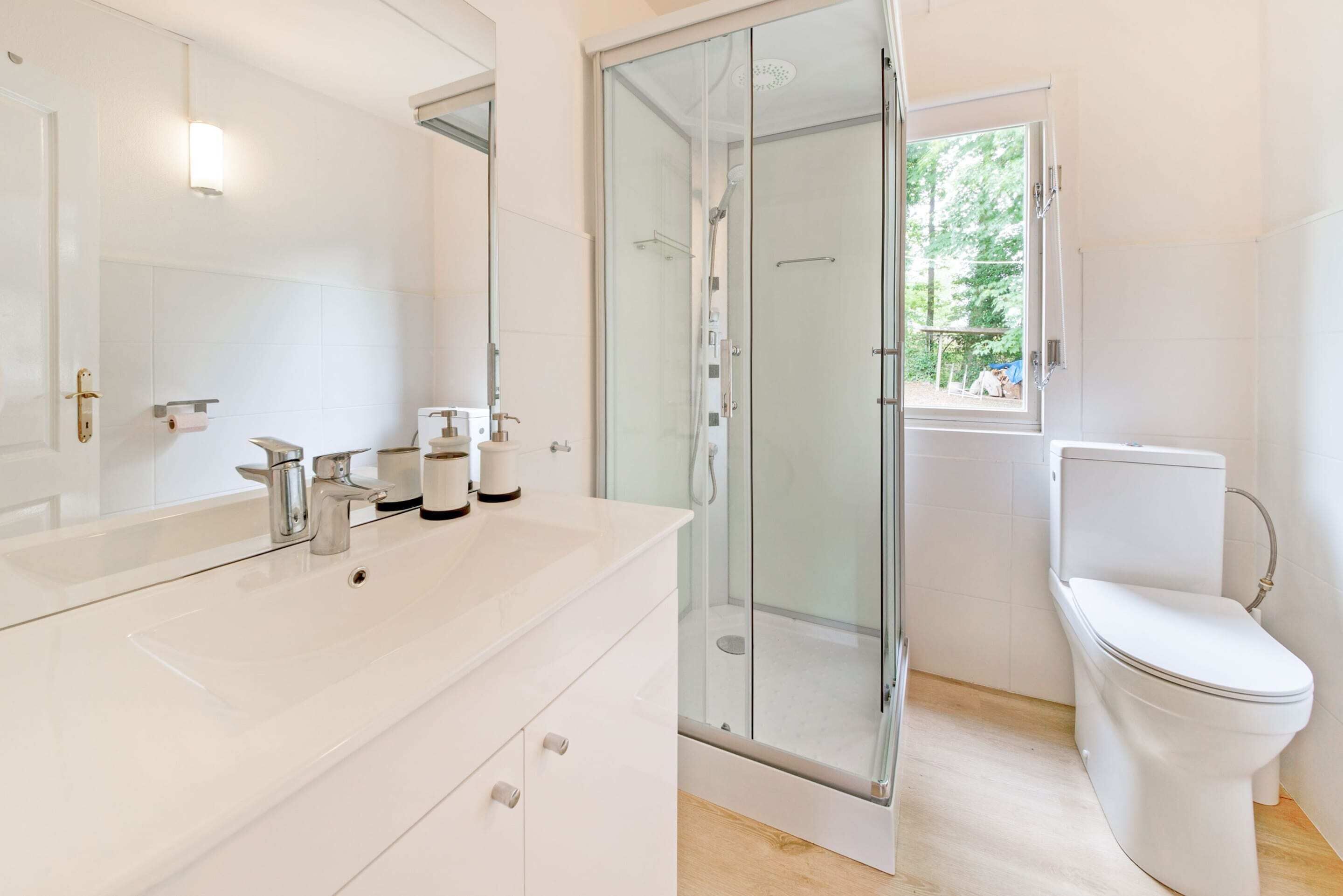 Un baño moderno con cabina de ducha de vidrio, inodoro blanco y un espejo grande sobre el lavamanos.