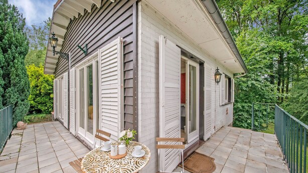 A small, single-story building with a patio area featuring a round table with a white patterned tablecloth, a chair, and a small potted plant. - Cozy Hideaway in Ferrieres (Ferrieres)