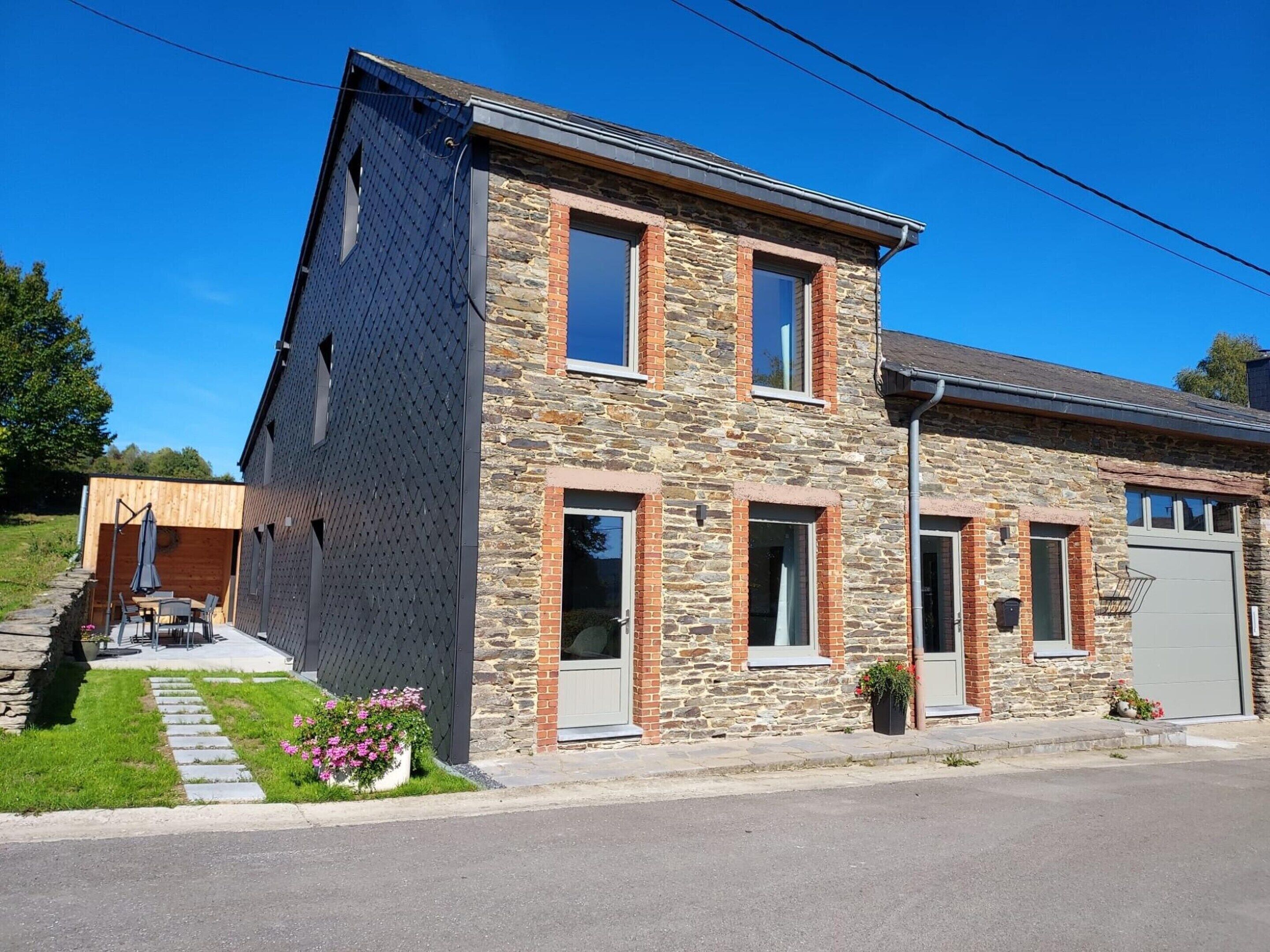 A two-story house with a stone facade, a garage, and a small garden with pink flowers.