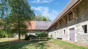 Ein Steinhaus mit geneigtem Dach und Holzbalken, ein Picknicktisch und ein Baum im Vordergrund.