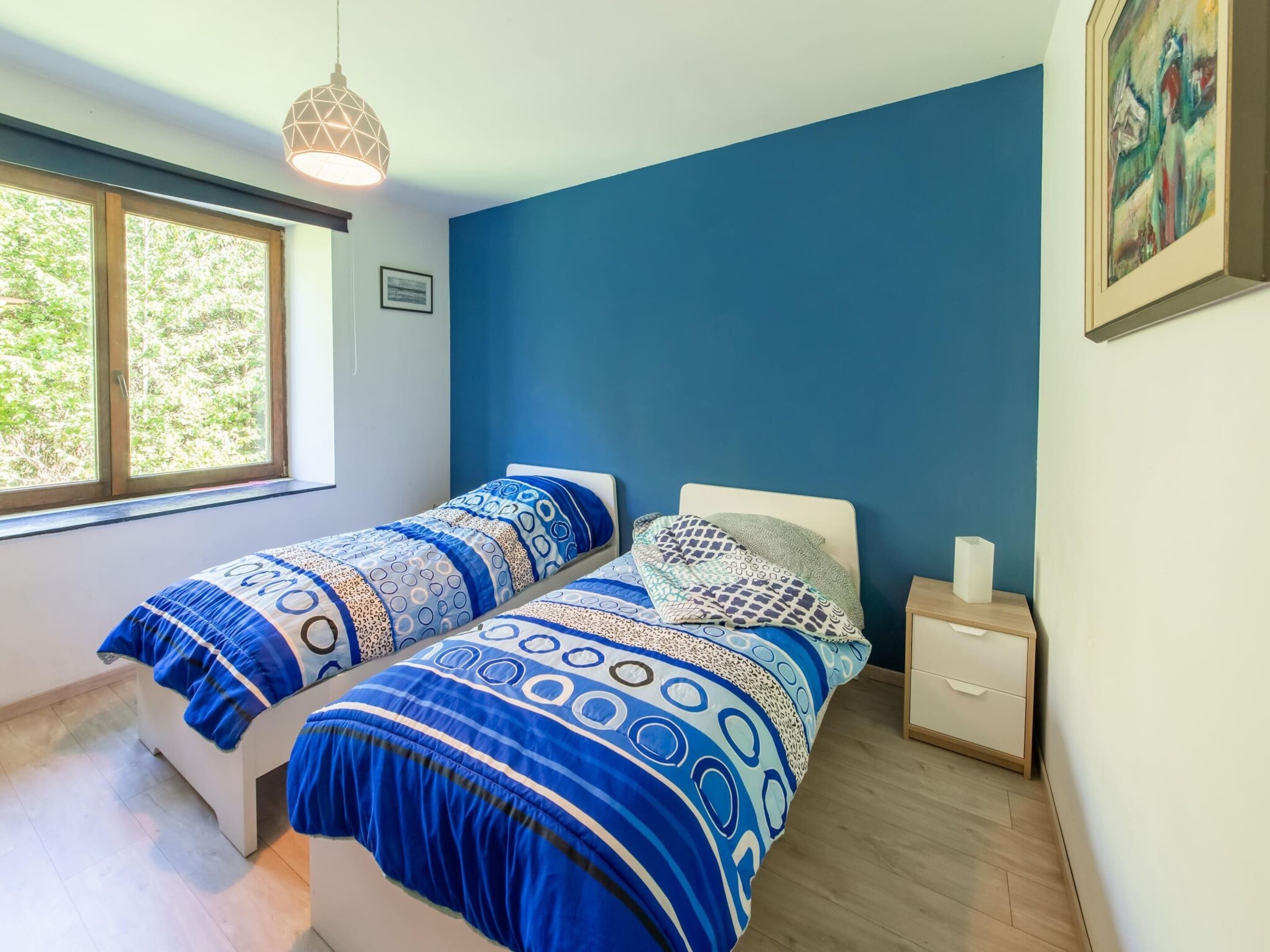Un dormitorio con dos camas, una ventana, una mesita de noche y una lámpara colgante.