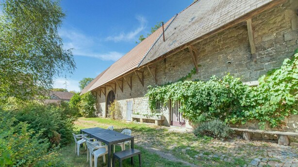 Ein Steinhaus mit Ziegeldach und einer überdachten Außenbereich-Sitzgruppe.
