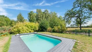 Ein rechteckiger Pool mit Holzterrasse, umgeben von üppiger Vegetation und Bäumen.