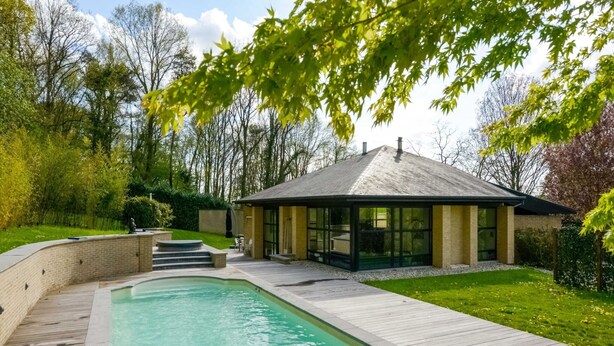Ein modernes Haus mit Schwimmbad, überdachter Terrasse und gepflegtem Garten.