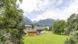 Ländliche Umgebung mit einem grünen Feld, Holzbauten und Bergen im Hintergrund.