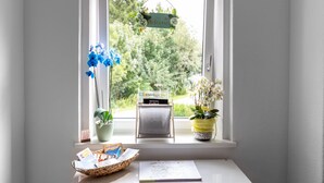 Ein Fenster mit einem Willkommensschild, zwei Blumentöpfen, einem Korb voller Karten und einem kleinen Tisch mit einem Notizbuch.