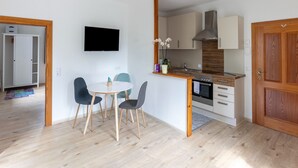 Eine moderne Küche mit Einbauofen, ein Essbereich mit rundem Tisch und Stühlen sowie ein an der Wand befestigter Fernseher.
