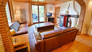 A cozy living room with a fireplace, leather sofa, and a television. - Chalet in Biron With Large Garden Near Durbuy (Erezee)