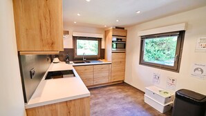 A modern kitchen with wooden cabinets, a stainless steel range, and a window with a view of greenery. - Chalet in Biron With Large Garden Near Durbuy (Erezee)