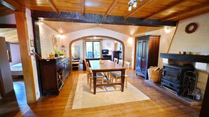 A cozy dining area with a wooden table and chairs, a fireplace, and a kitchen in the background. - Chalet in Biron With Large Garden Near Durbuy (Erezee)