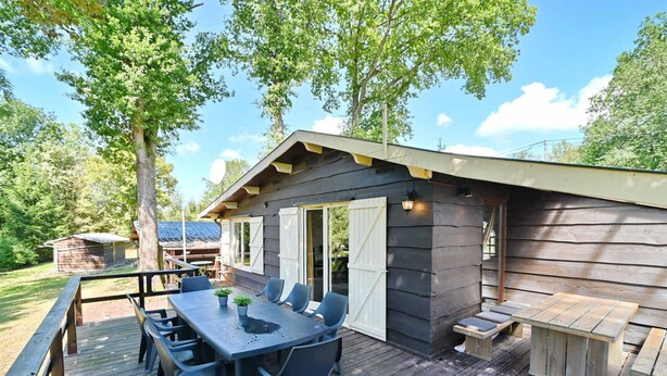 A wooden deck with a table and chairs, a small wooden structure, and a covered area with a door. - Chalet in Biron With Large Garden Near Durbuy (Erezee)