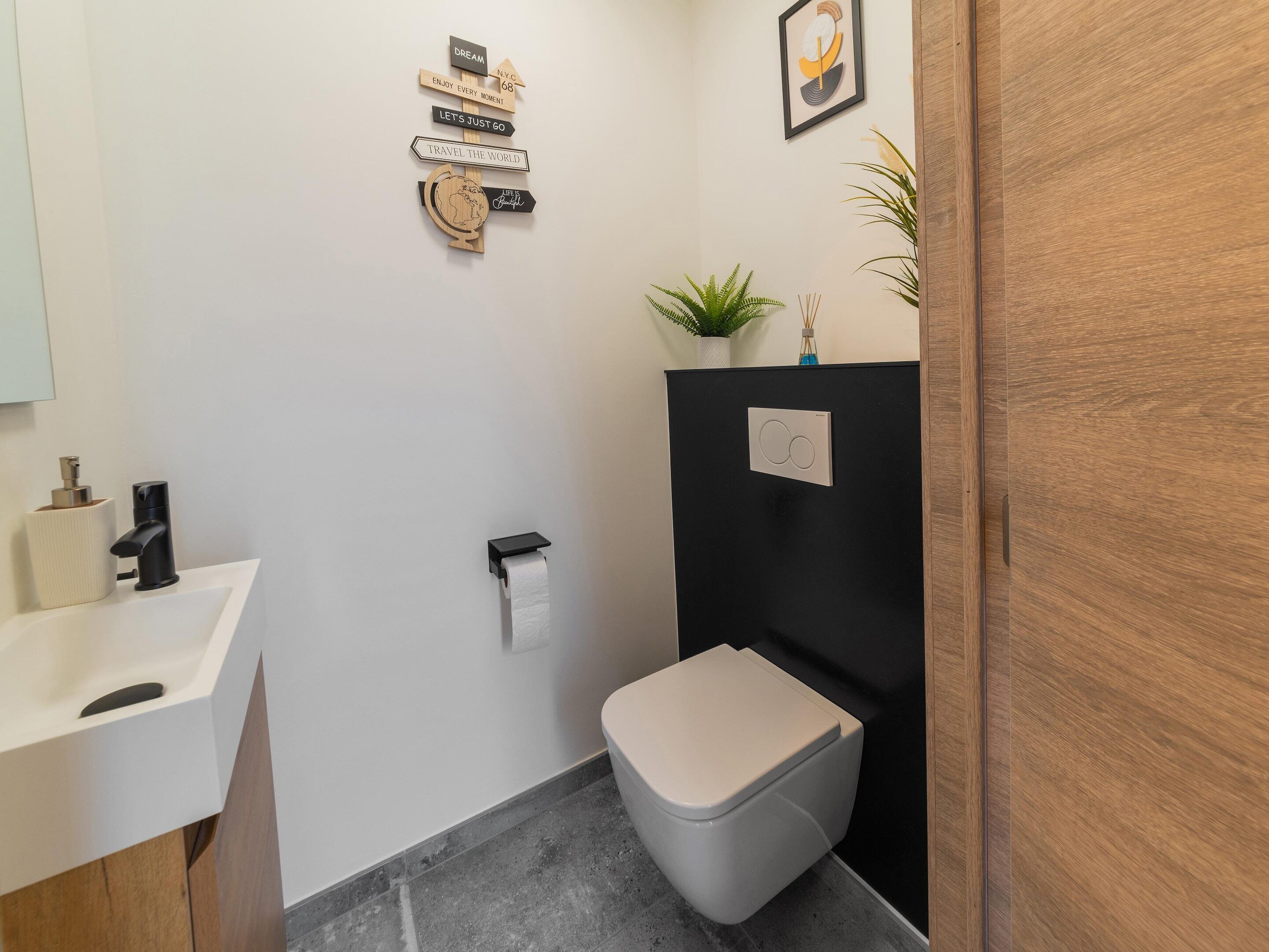 A modern bathroom with a toilet, sink, and a wall-mounted sign with motivational phrases.