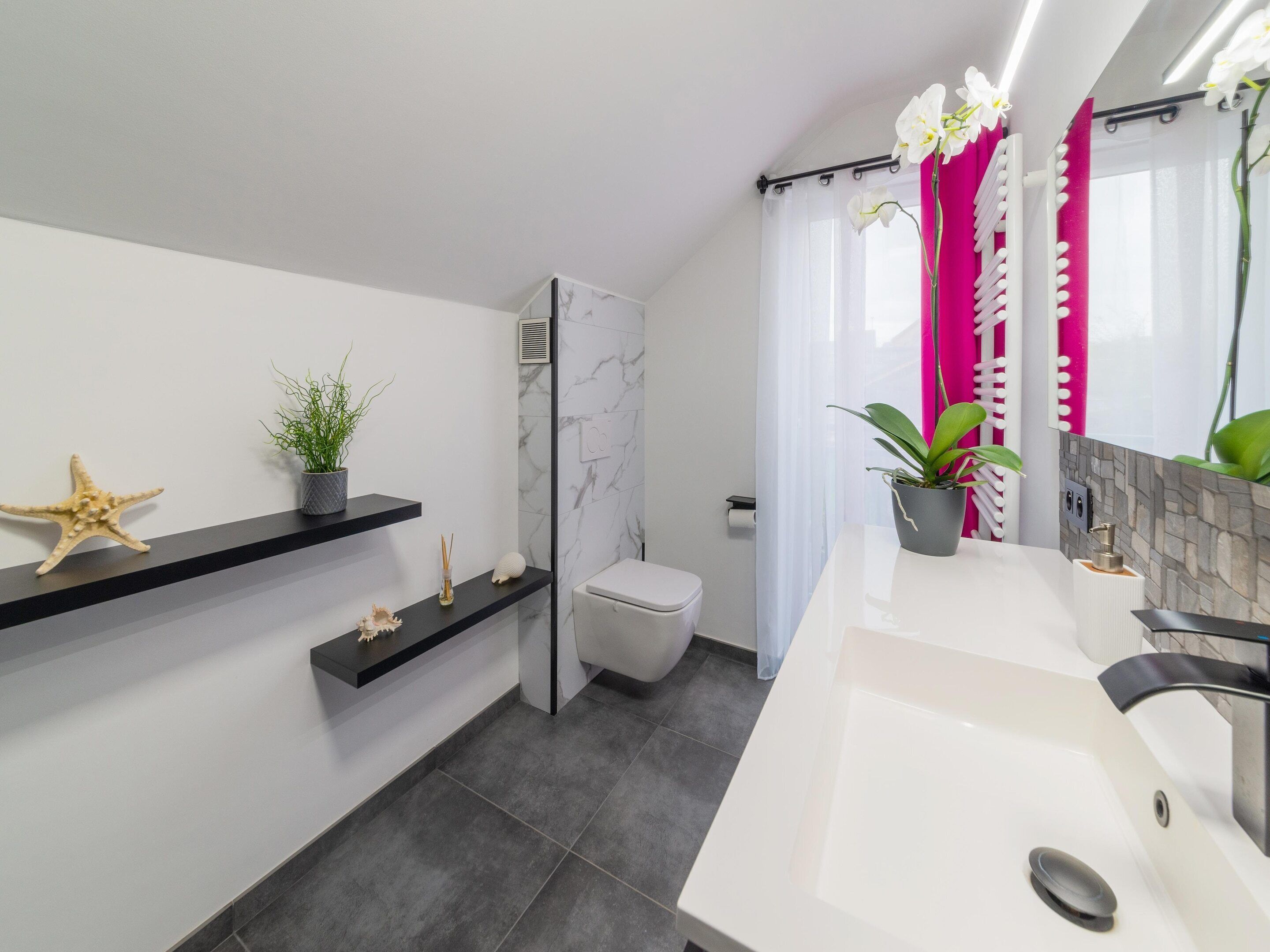 Ein modernes Badezimmer mit einem weißen Waschbecken, schwarzen Regalen, einer Toilette und einer Duschkabine.