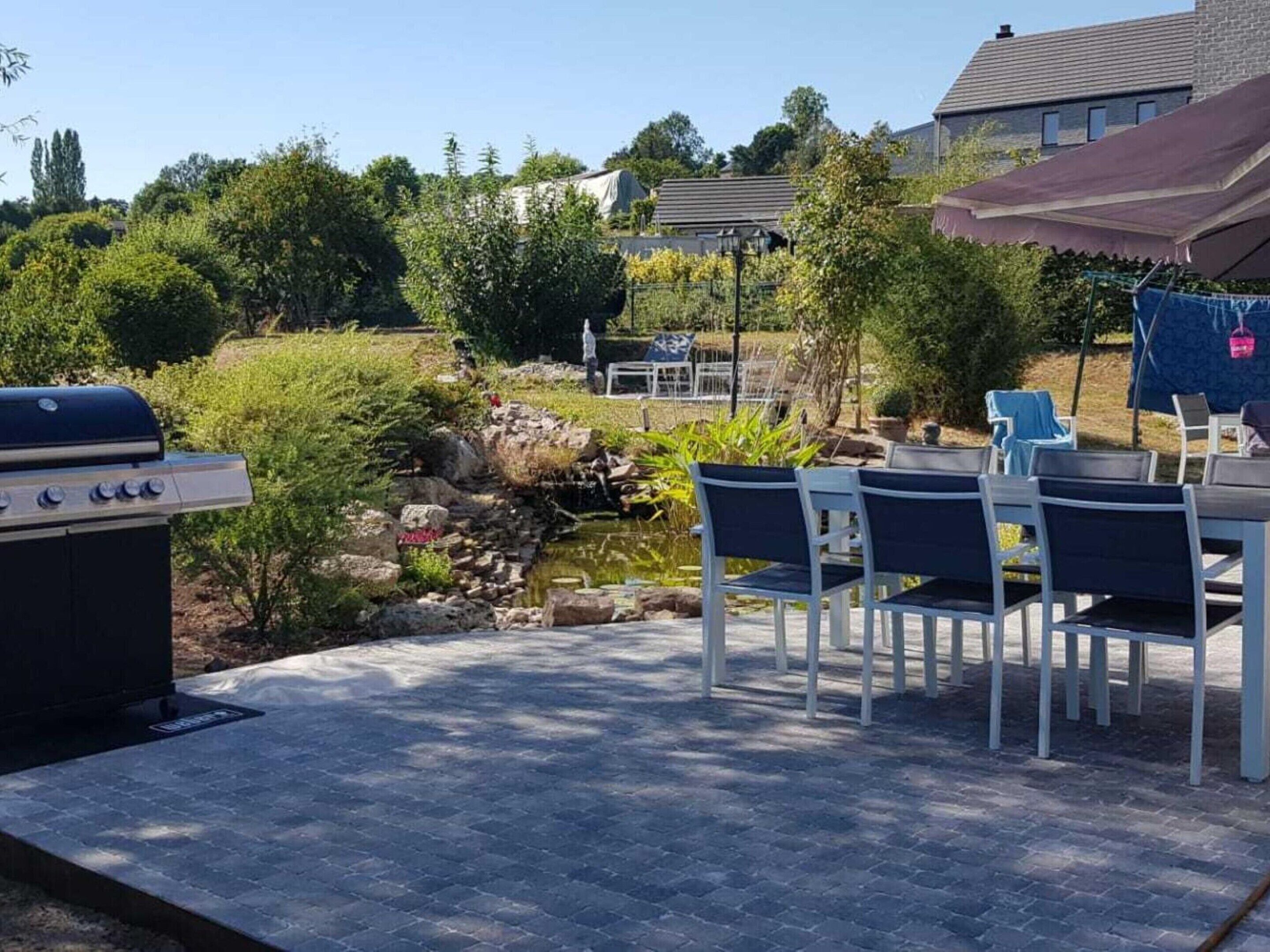 Une terrasse avec un barbecue, des sièges d’extérieur et un petit étang.