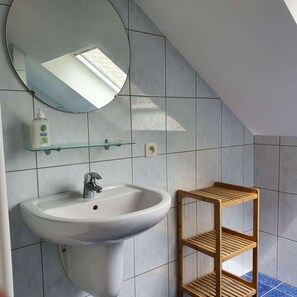 Une salle de bain avec un lavabo blanc, un miroir et une étagère en bois.