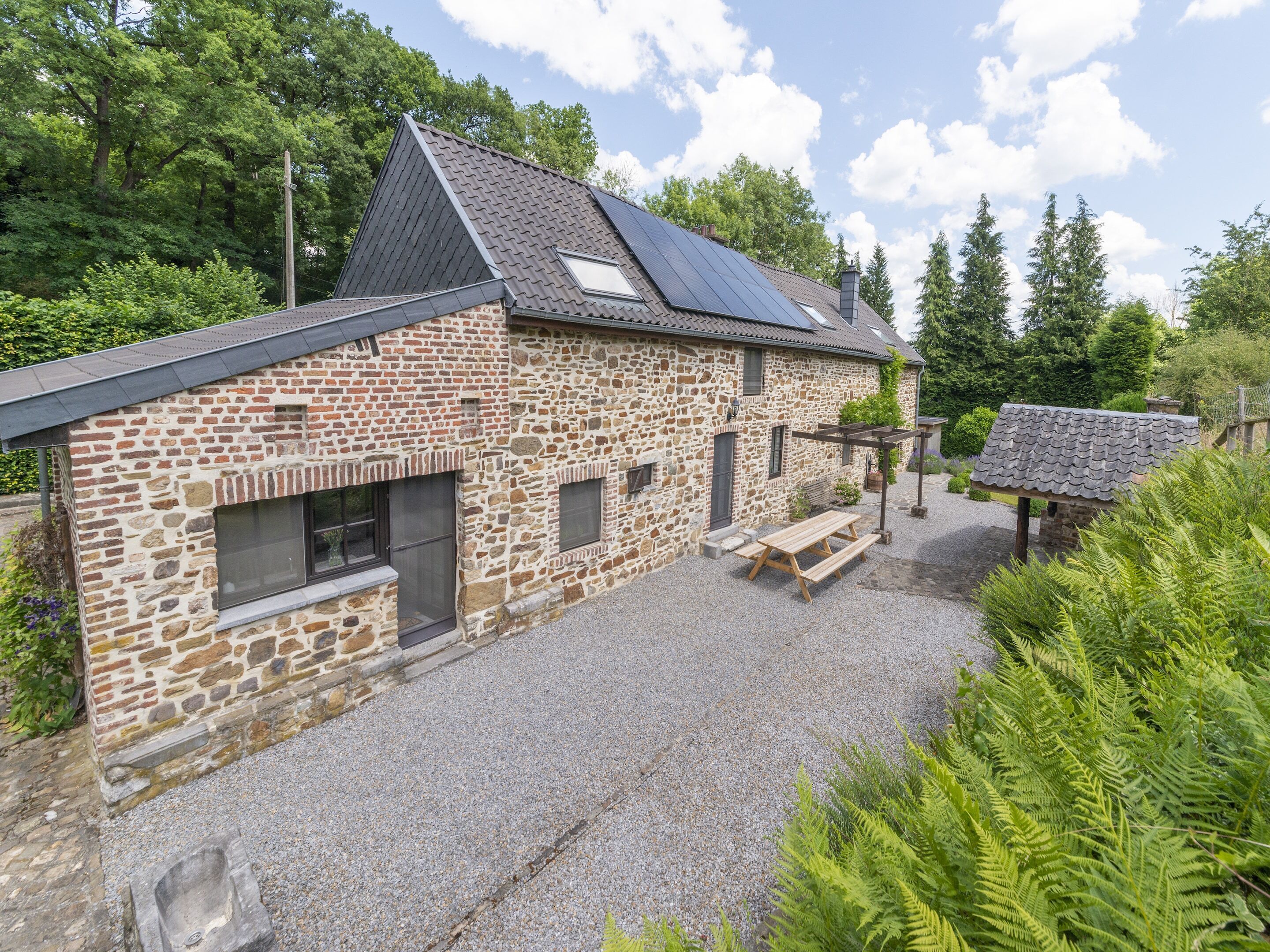 A stone building with a sloped roof, solar panels, and a gravel patio.
