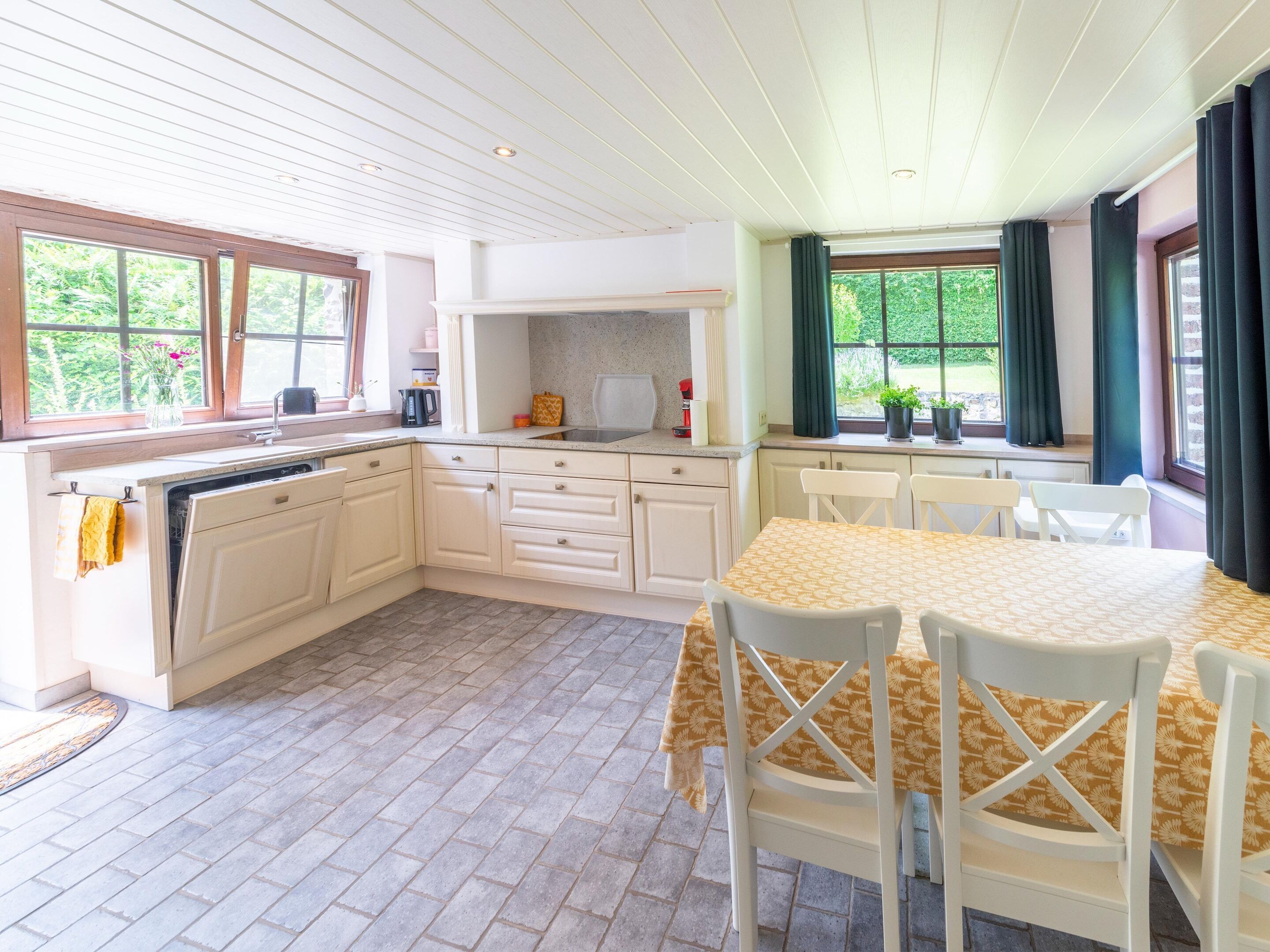 A kitchen with white cabinets, a dining table with chairs, and a window with curtains.