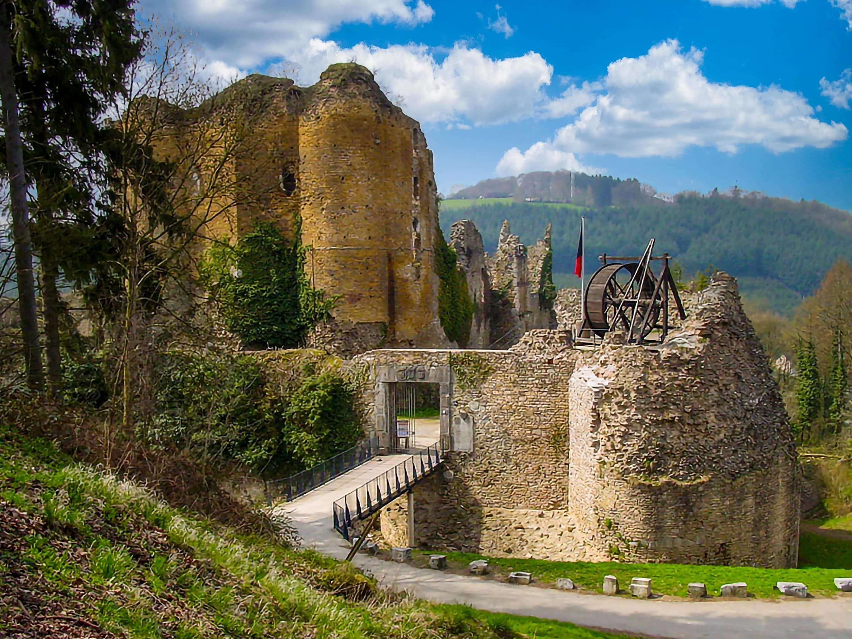 Une structure historique en pierre, avec une rampe menant à une porte, entourée de verdure et sous un ciel dégagé.