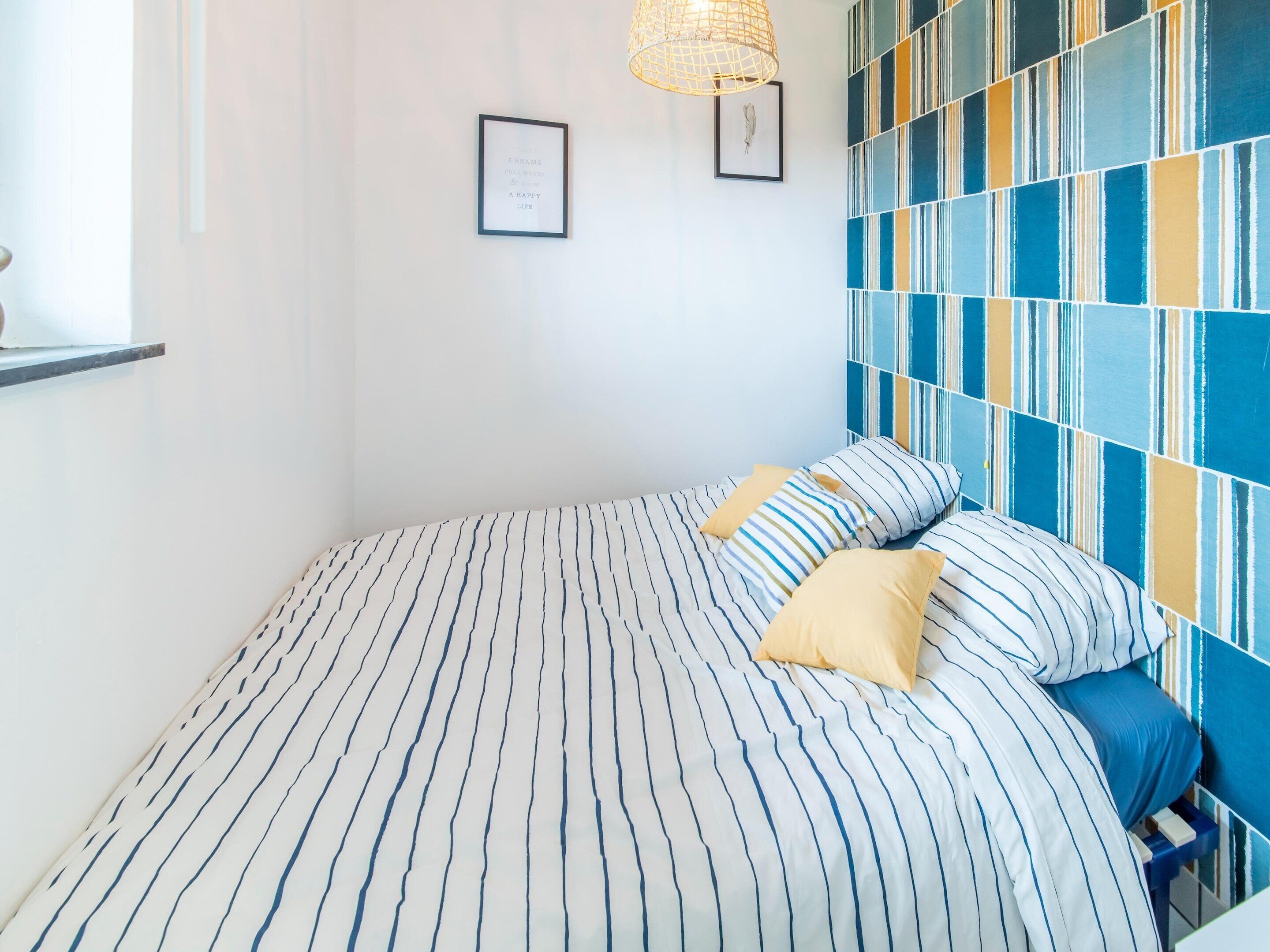 A bed with striped bedding, a blue and yellow patterned wall, and a framed picture on the wall.