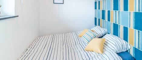 A bed with striped bedding, a blue and yellow patterned wall, and a framed picture on the wall.