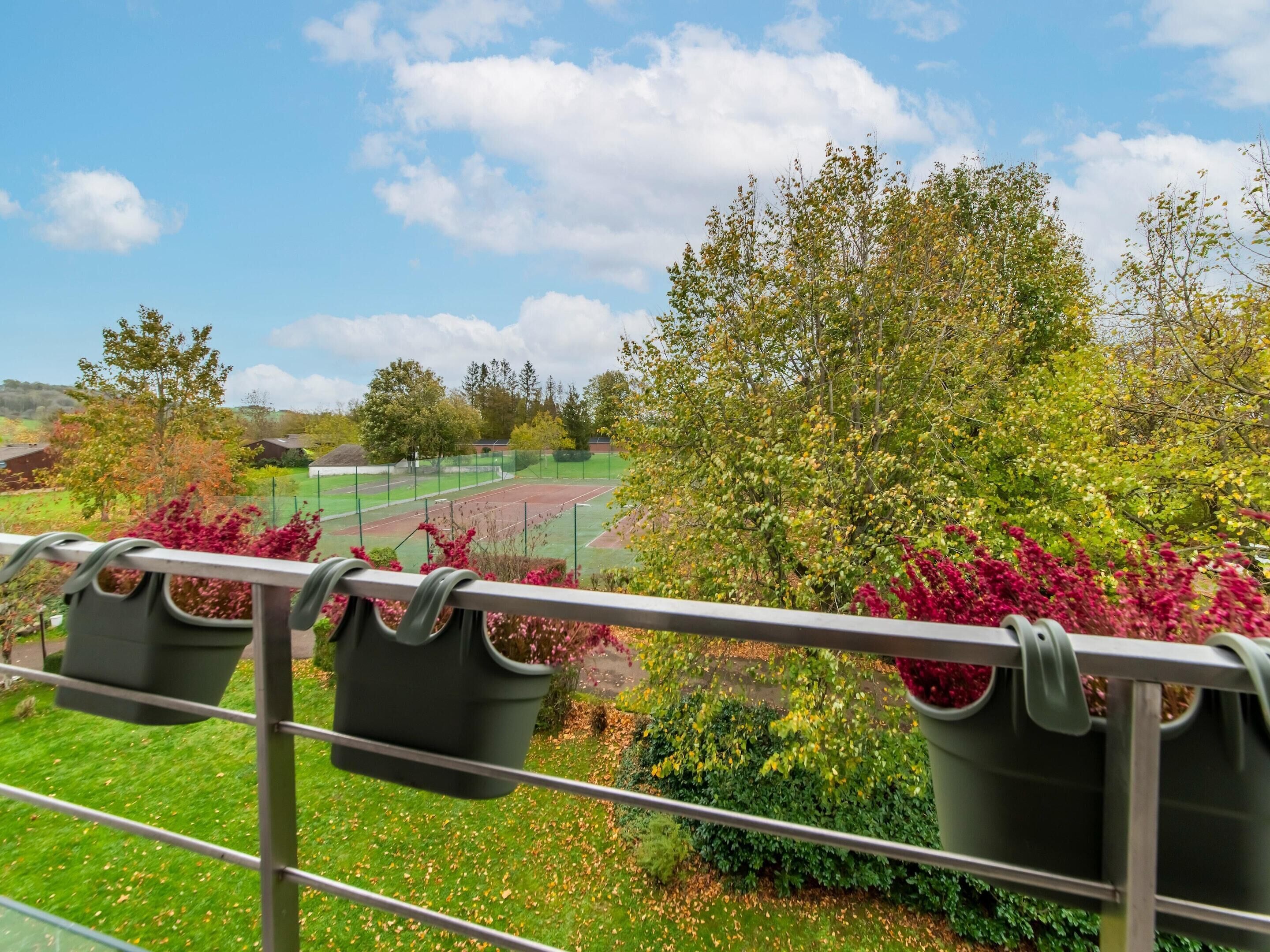 A tennis court with surrounding greenery and a clear sky.