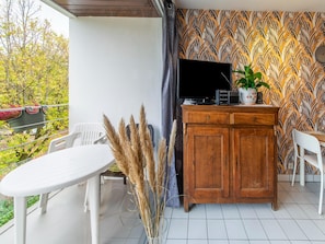 A balcony with a white table, chairs, a wooden cabinet, and a television.