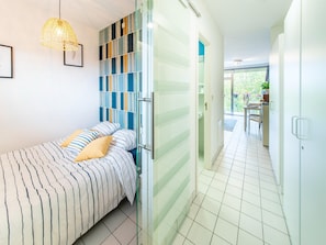 A bedroom with a bed, a hanging light fixture, a striped headboard, and a view of a balcony.