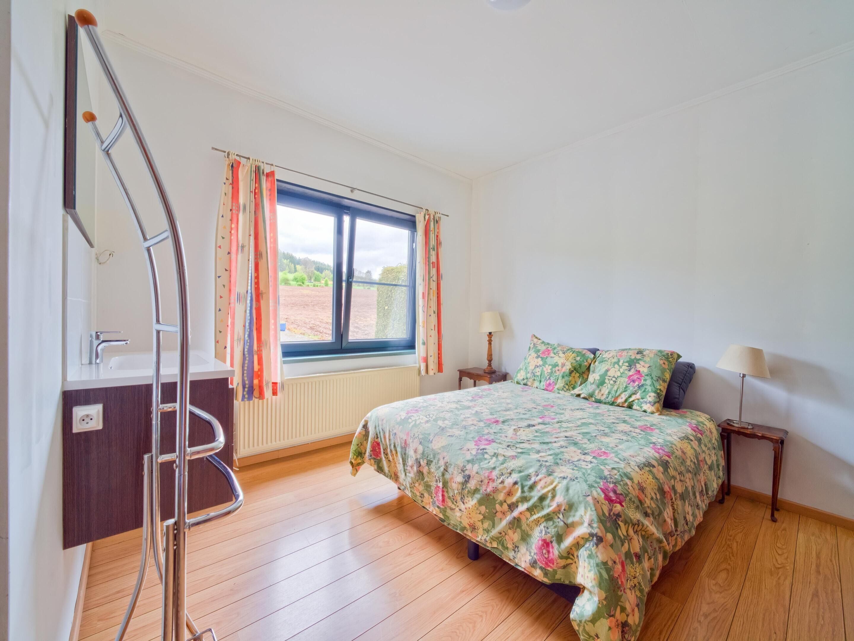 A bedroom with a bed, two bedside tables, a window with curtains, a radiator, and a wooden floor.