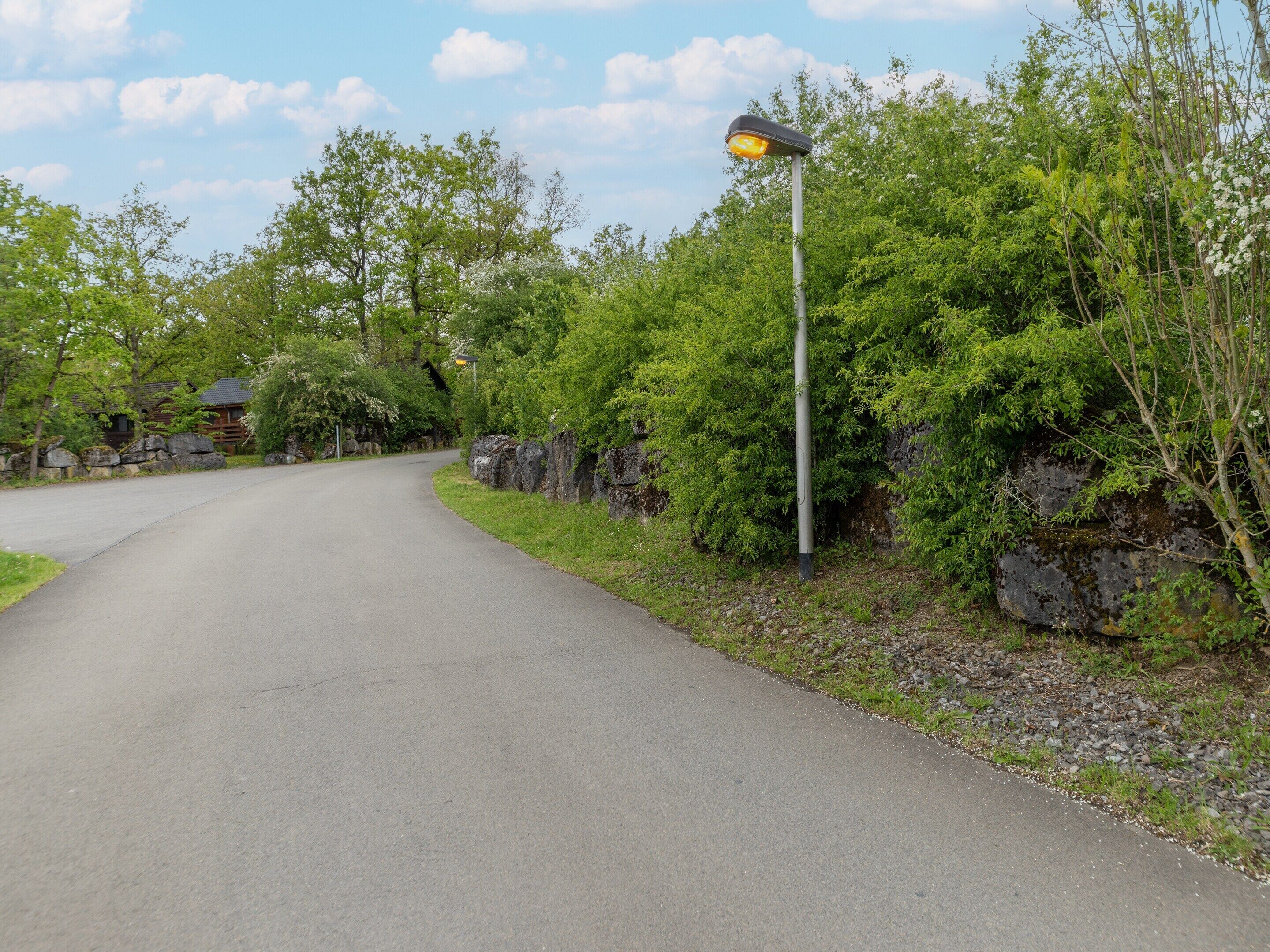 A paved road curving through a wooded area with a house in the background.