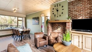 Un salon spacieux doté d’une cheminée en briques, d’une grande horloge murale et d’un coin repas offrant une vue sur l’extérieur.
