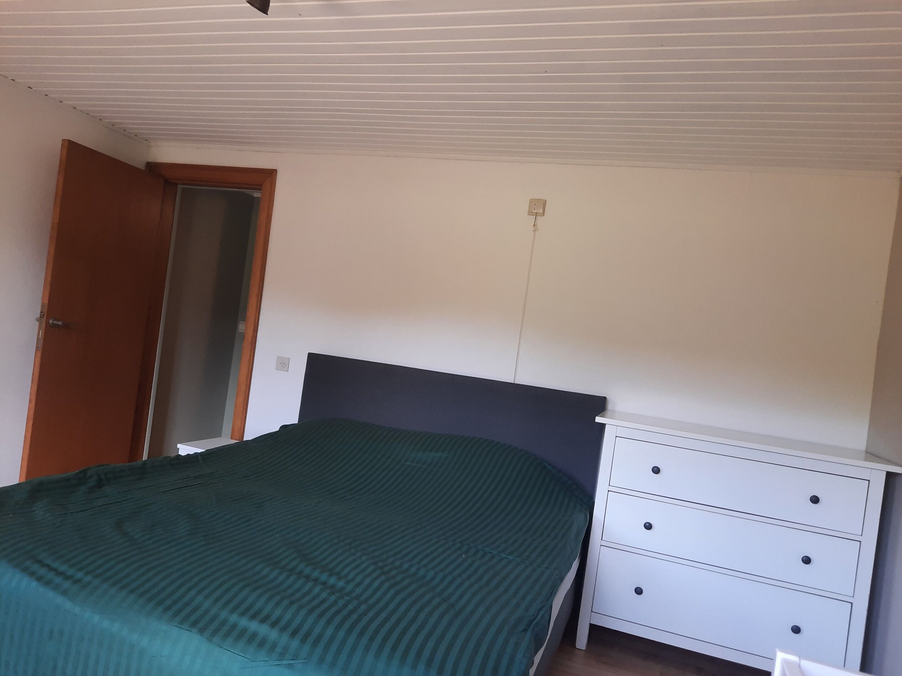 A bedroom with a bed, a white dresser, and a door.