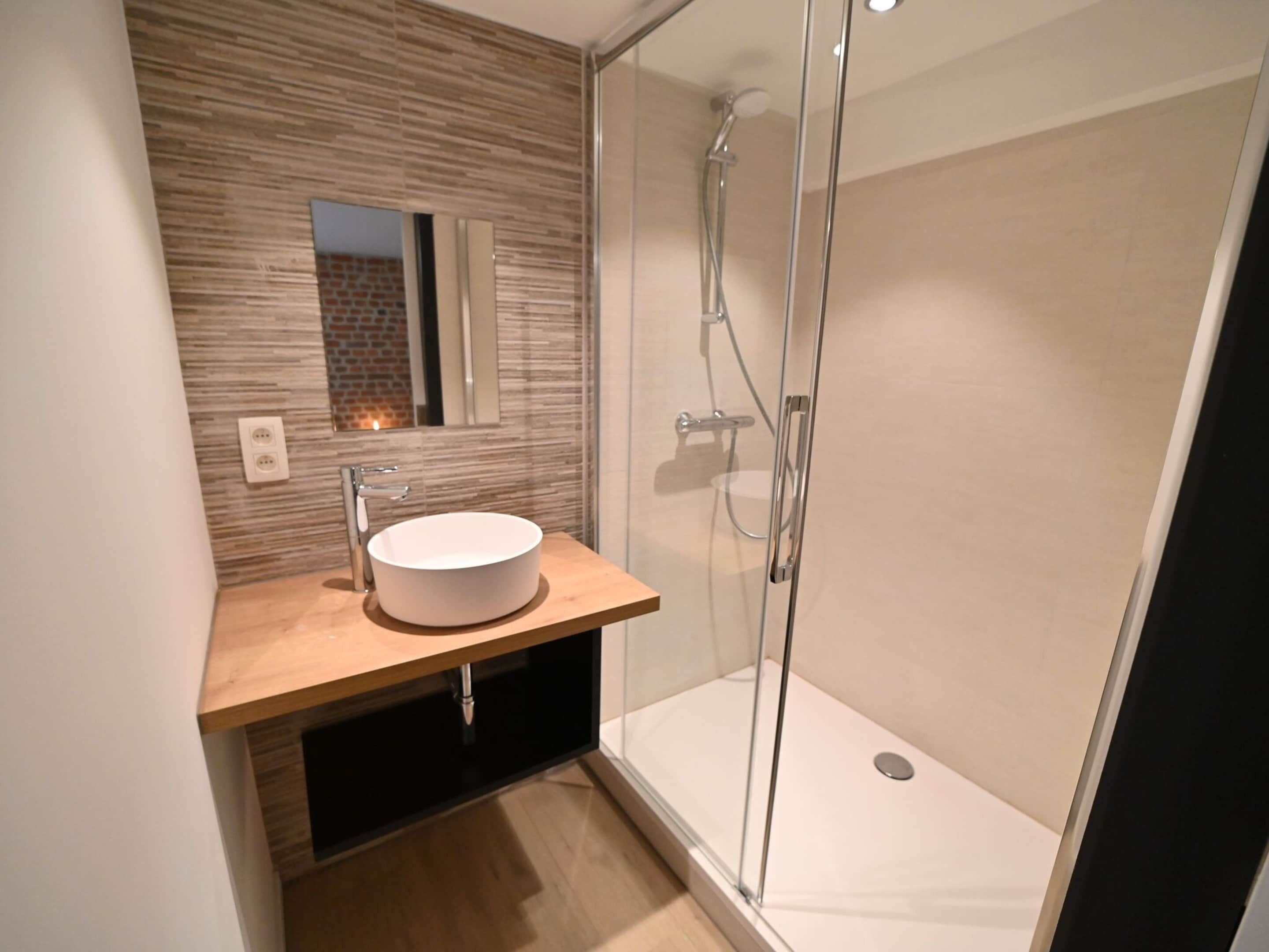 Une salle de bain moderne avec un lavabo rond, une cabine de douche en verre et un meuble-lavabo en bois.