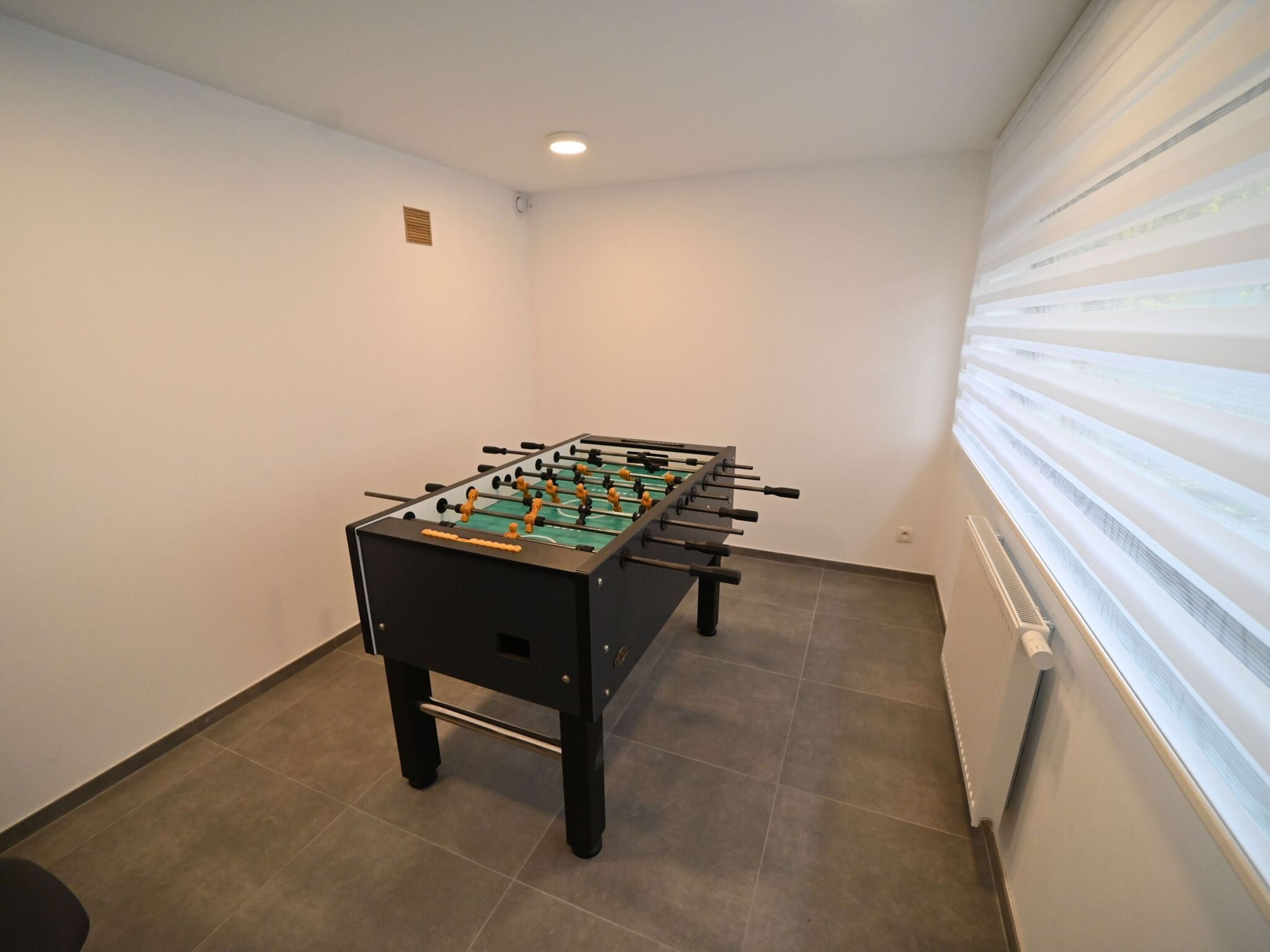 A room with a foosball table, a radiator, and a window with blinds.