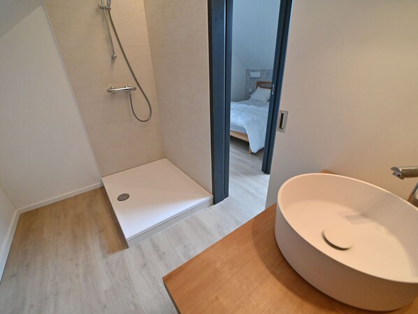 Un baño moderno con ducha, lavamanos y suelo de madera.