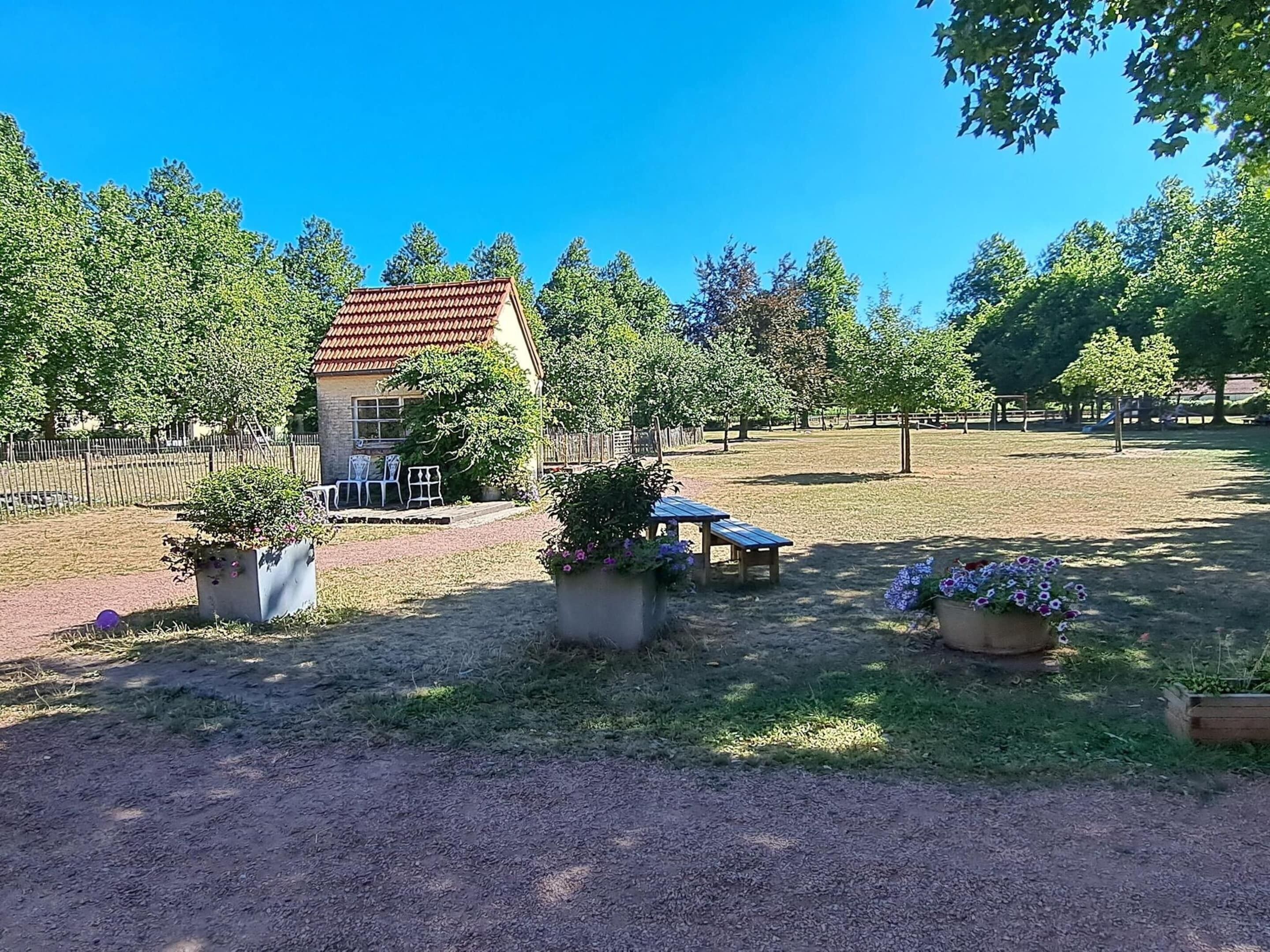 A house with a red roof, surrounded by a fenced yard with a picnic table and potted plants.
