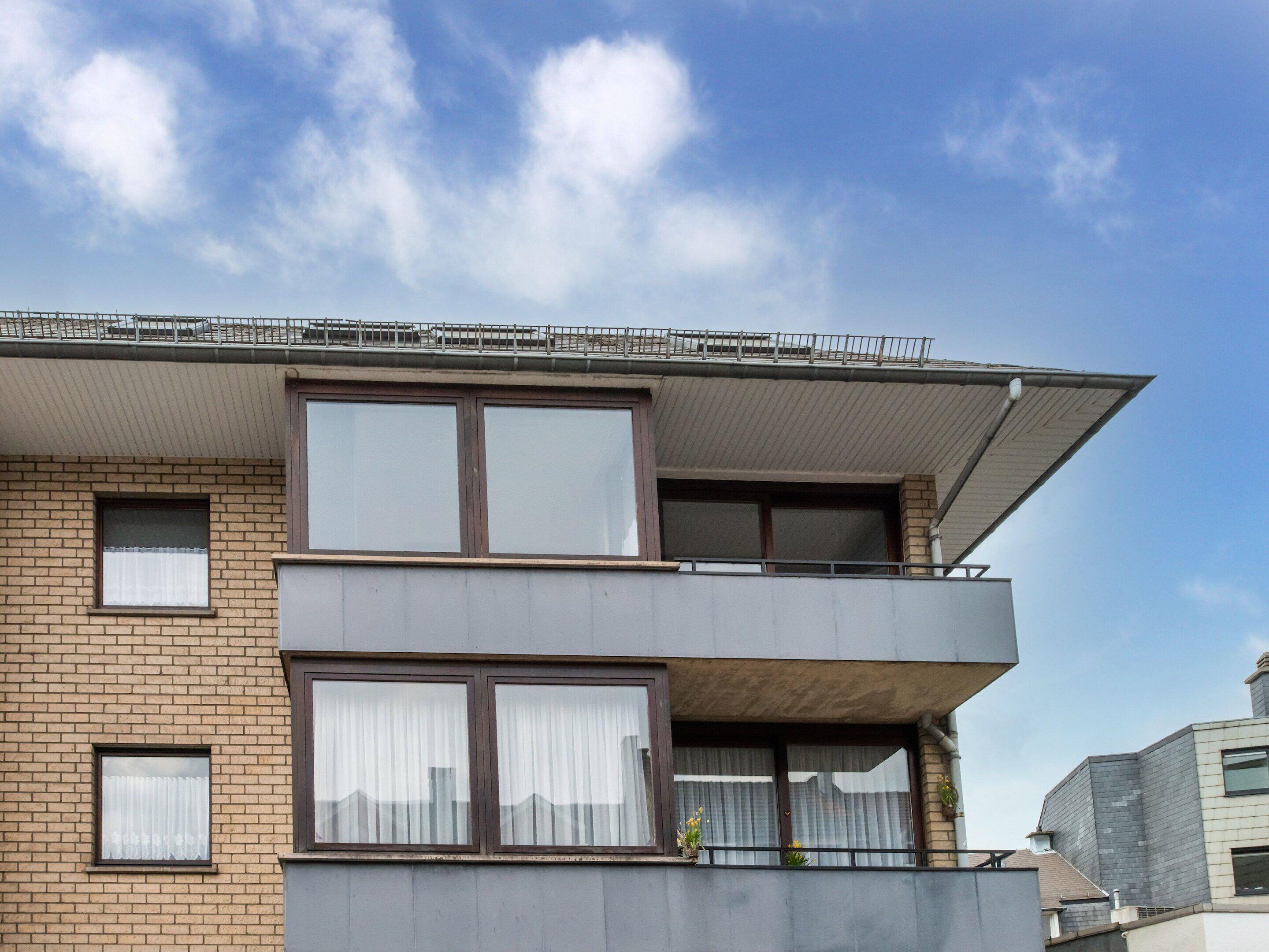 Un edificio moderno de dos plantas con ventanas grandes, un balcón y techo plano.