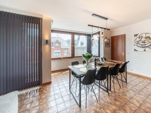 Un comedor con una mesa preparada para cuatro personas, un jarrón con flores y vista a un edificio de ladrillo a través del ventanal.
