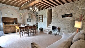 Un interior rústico con pared de piedra, vigas de madera, zona de comedor y un espacio de sala de estar acogedor con sofá.