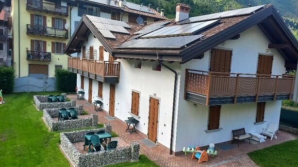 Un bâtiment de style chalet, doté d’un toit en pente, d’un espace extérieur aménagé avec des tables et des chaises, et d’un chemin de pierre menant à l’entrée.