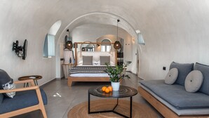 A modern interior with a bed, sofa, and a small table with oranges. - Almyra Oia Suites Adults Only  (Santorini)