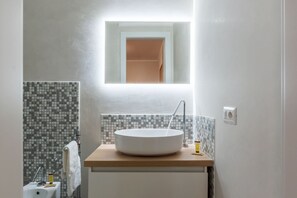 Een badkamer met een rond wastafel, een spiegel erboven en een betegelde spatwand.
