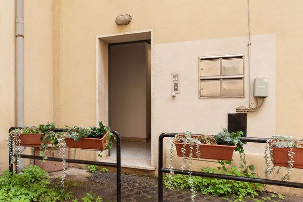 A building entrance with a door, a window with a light fixture, and potted plants on the ground.