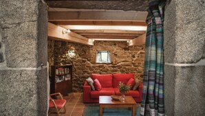 A cozy room with a stone wall, a red sofa, a wooden coffee table, and a bookshelf. - One of two private and intimate casitas. Surrounded by nature. (Moraña)