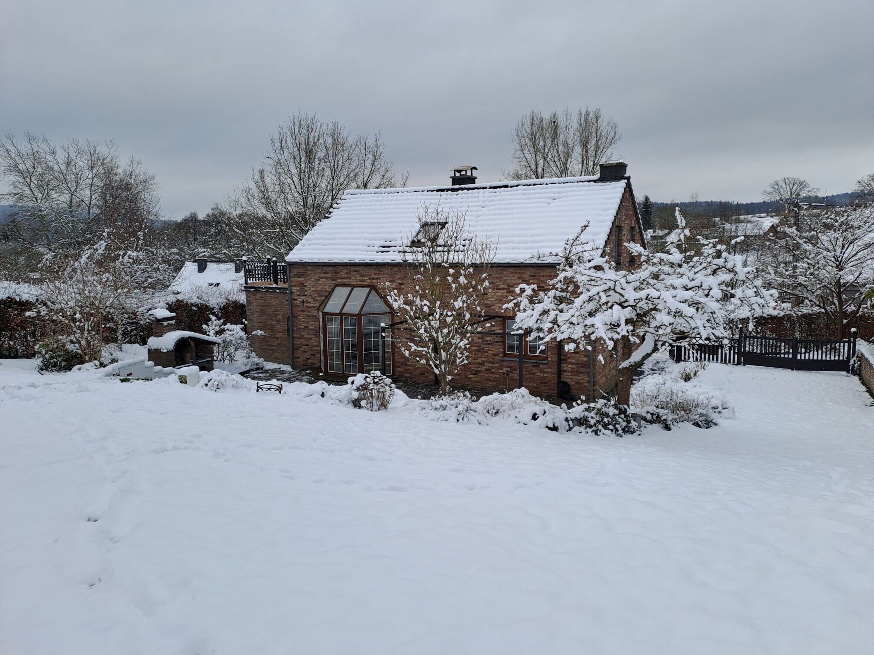 A brick house with a snow-covered roof and a small garden area.