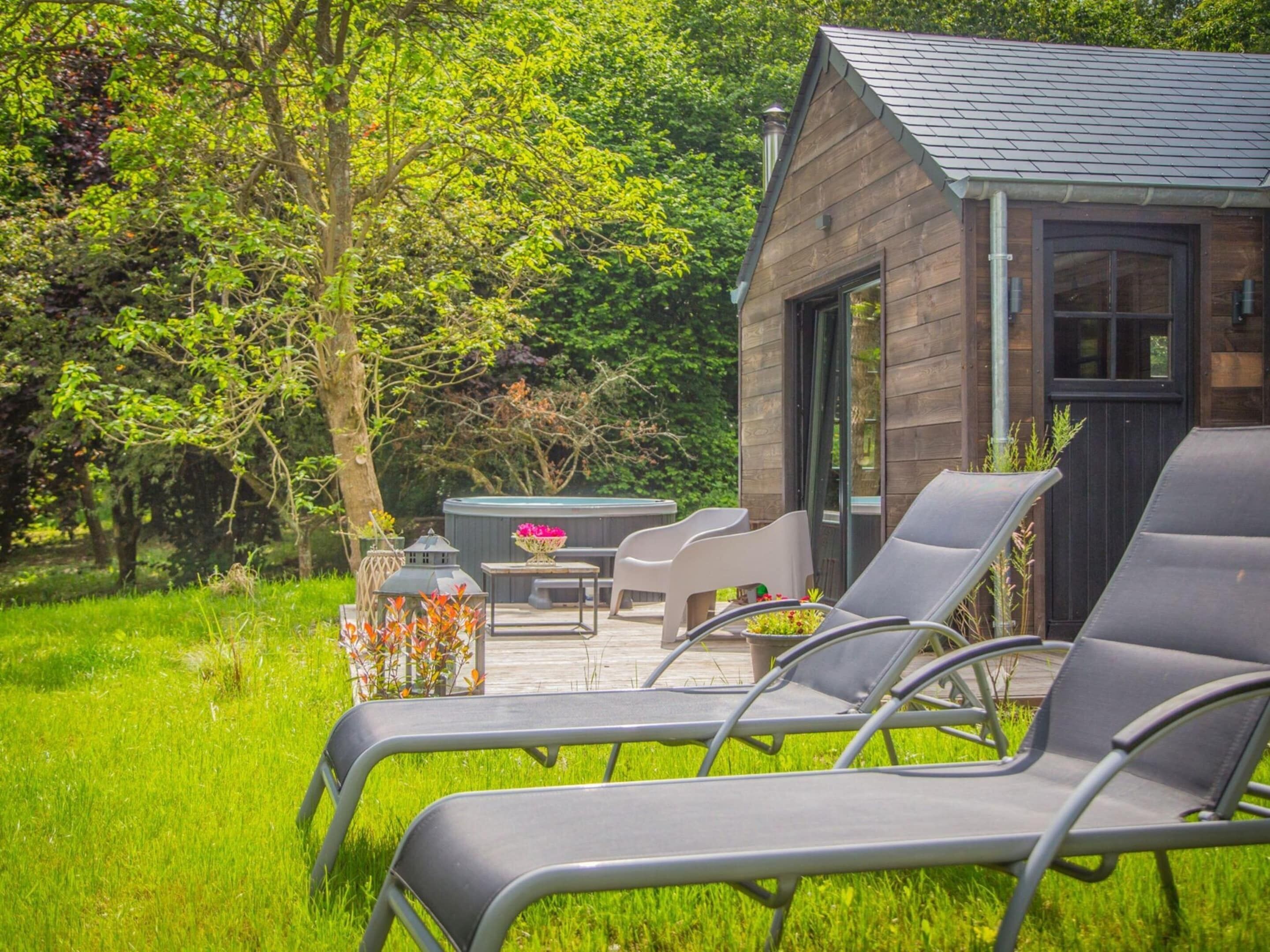 Una pequeña cabaña de madera con un patio que incluye sillones de descanso y una mesa con un arreglo floral.