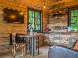 A rustic cabin interior with a wooden dining table, a single chair, a sofa, and a TV mounted on the wall. - Holiday Home in Ferrieres With Garden (Ferrieres)