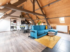 An attic-style living room with a blue sofa, dining table, and chairs. - Apartment in Wortel Hoogstraten With Garden (Hoogstraten)